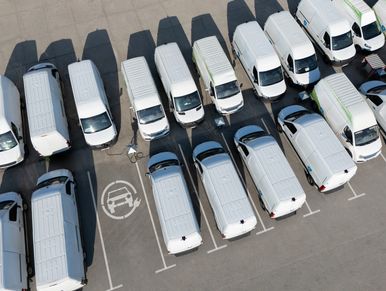 Aerial view of white vans parked in marked spaces in a lot.