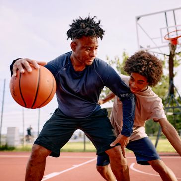 Two young men playing basketball outdoors.