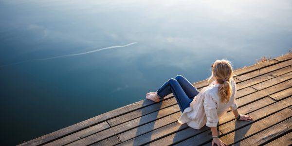 Person sitting on a wooden dock overlooking calm water.