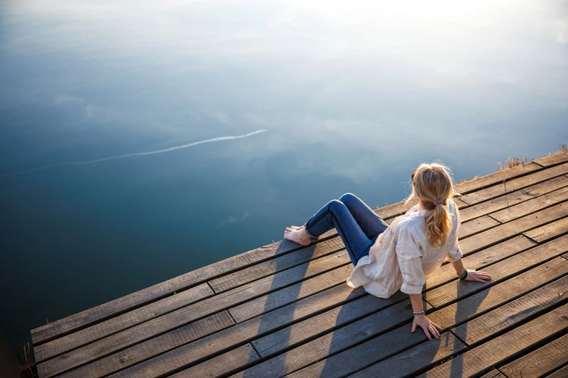 Woman relaxing on pier. Tranquil lake scenery and mindfulness moment in nature