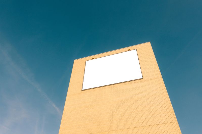 Large blank billboard on a brick wall with blue sky background providing advertising space