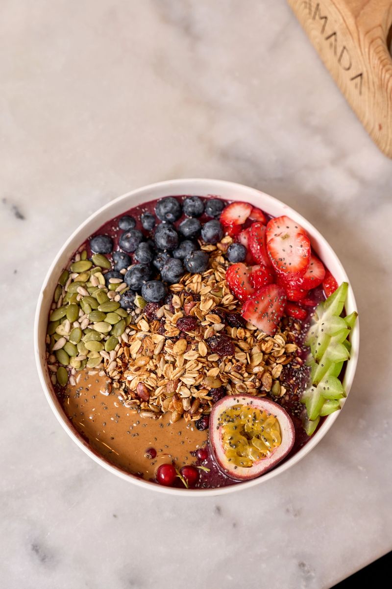 Healthy and colorful acai bowl made with various fruits, granola, seeds, peanut butter, and chia seeds