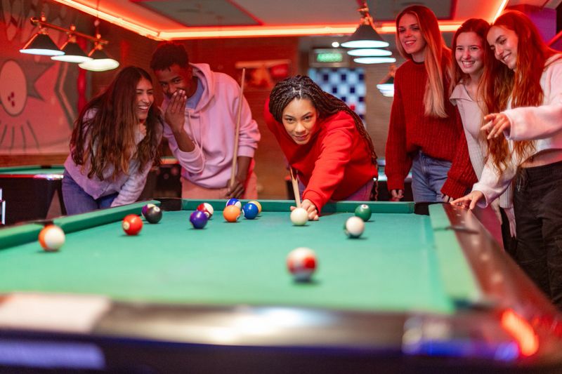 Young woman takes her shot in billiards as her friends watch and cheer her on in a vibrant pool hall