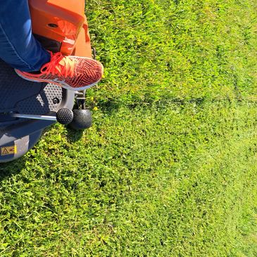 Person wearing red shoes sitting on an orange mower on green grass.