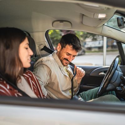 Man fastening seatbelt in car while woman watches.