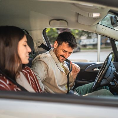 Man fastening seatbelt with woman in passenger seat.