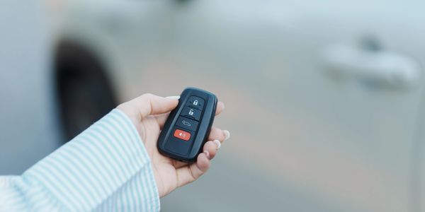 Person holding a car key fob near a white vehicle.