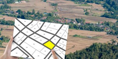 Person holding a land plot map with one plot highlighted in yellow.