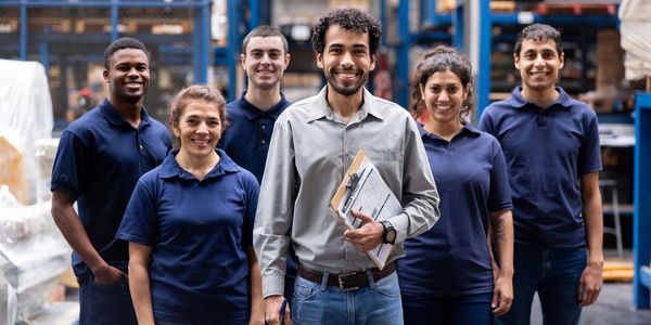 A diverse team of six warehouse workers smiling and standing together.
