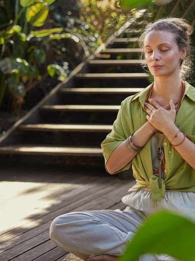 Woman meditating peacefully outdoors on wooden deck near stairs.