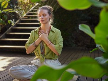 Woman practicing mindfulness meditation outdoors with eyes closed and hands on chest.