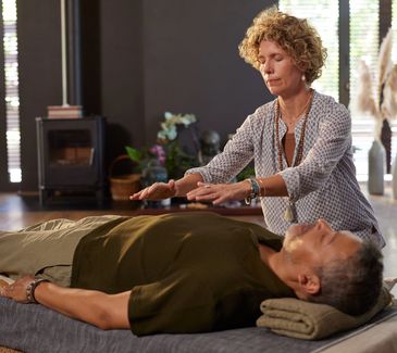 A woman performing Reiki healing on a man lying down.
