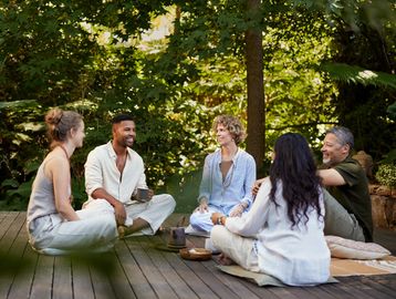 Five people sitting in a circle outdoors, enjoying a conversation.