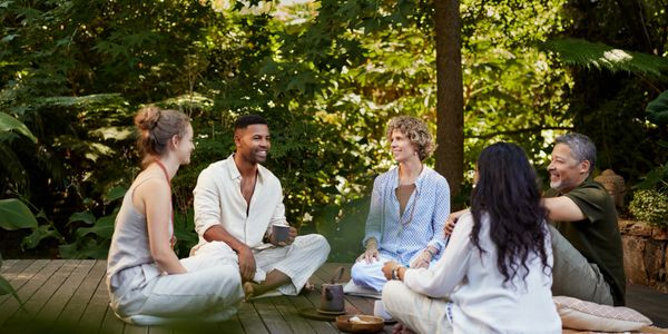Five people sitting on a wooden deck, enjoying a relaxed outdoor conversation.