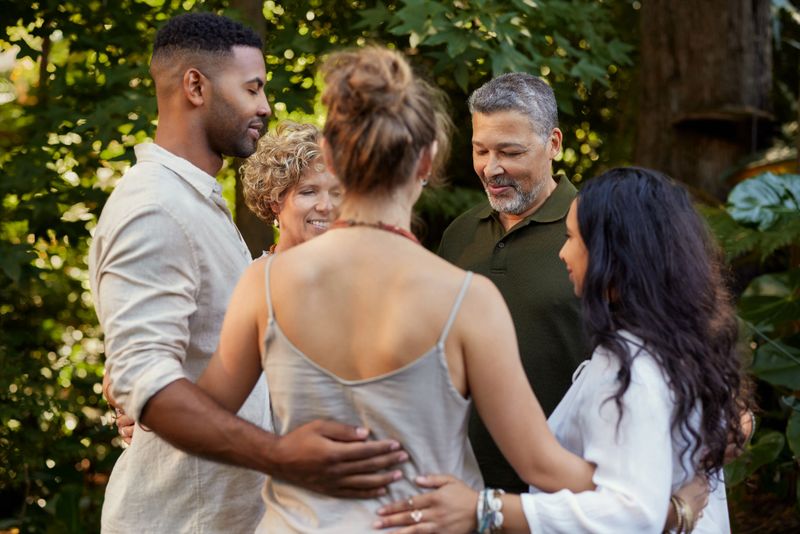 Diverse group of adults stands in circle, sharing a moment of connection and support at wellness retreat. Multiethnic friends stand in unity, after spiritual practice meditation. Mindful people standing in a circle giving support at holistic center after family constellations or systemic therapy.