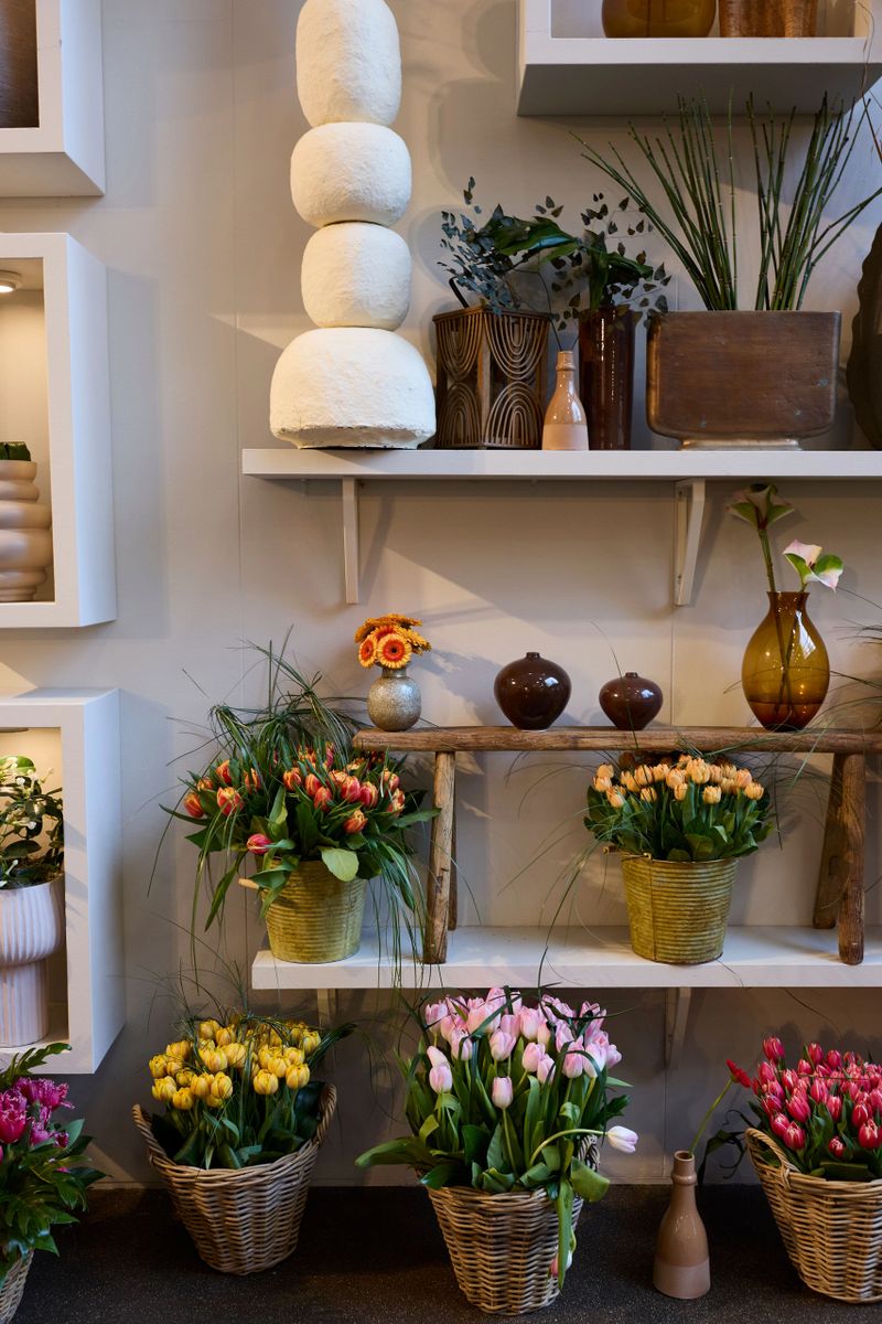A beautifully arranged flower shop display with colorful tulips in baskets and decorative vases on shelves.