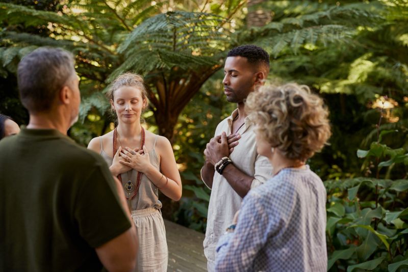 Group of multiethnic adults standing peacefully in circle with hands on their hearts during a wellness retreat in nature. Diverse people practice mindfulness and gratitude together in a forest. Mixed race group sharing a meditation on fourth chakra, heart chakra, outdoor with copy space.