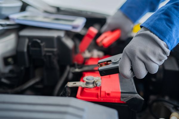 Person wearing gloves connecting jumper cables to a car battery.