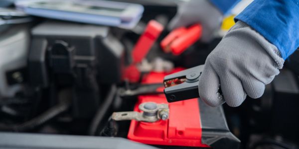 Person attaching jumper cable to car battery.