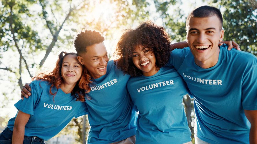 Four diverse young volunteers smiling and posing outdoors in blue shirts.