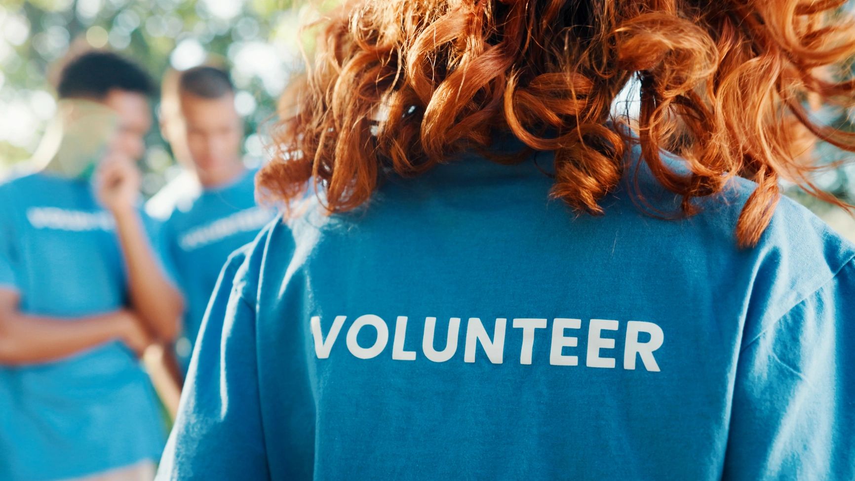 Person wearing a blue volunteer shirt with curly red hair.