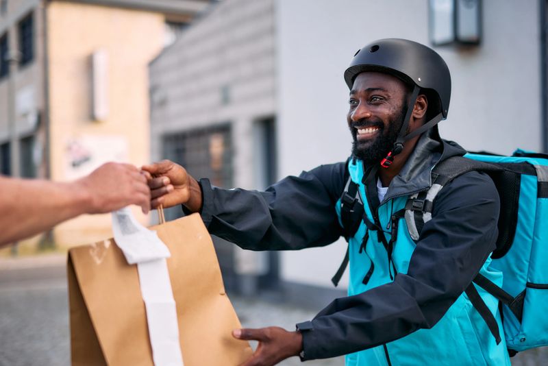 Cheerful courier wearing a helmet and backpack handing over a package to a customer, capturing the essence of efficient delivery service and modern logistics