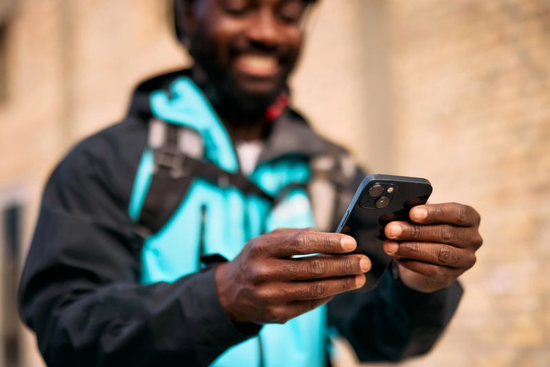 Delivery worker in a blue jacket checking smartphone for directions, emphasizing technology's role in modern logistics and the focus on efficient navigation