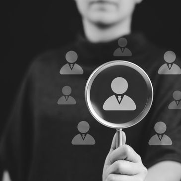 Person holding magnifying glass focusing on a business icon among others.