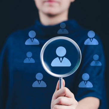 Person holding magnifying glass focusing on business icons representing recruitment.