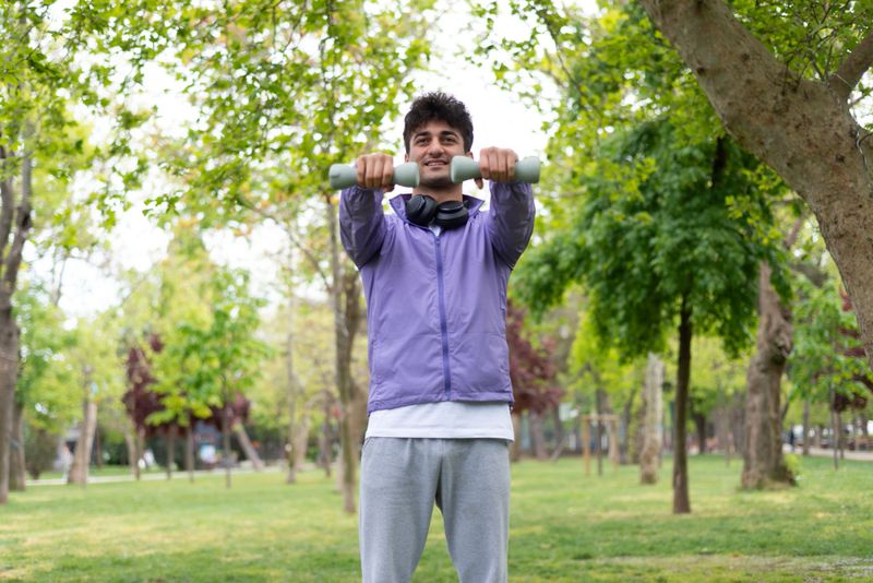 Young man exercising shoulder press outside with dumbbells