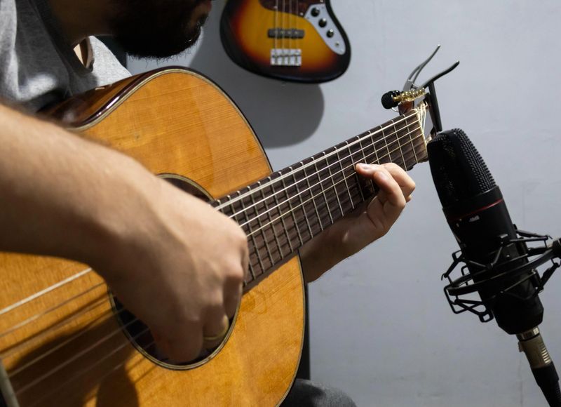 A musician concentrates on playing the guitar in a recording studio. The image captures the guitarist hand pressing the strings, while a recording microphone captures the sound.