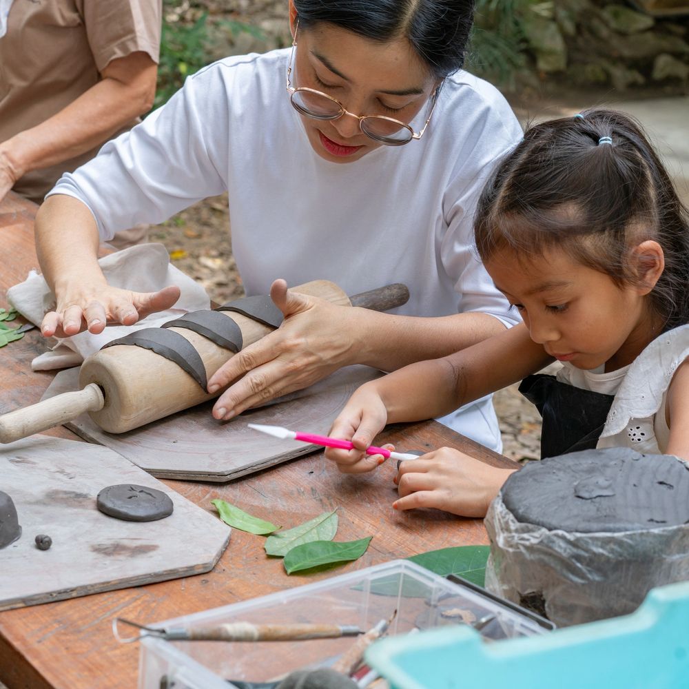 A woman and a girl engaged in clay crafting with tools and leaves on the table.