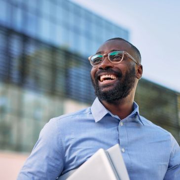 Smiling man holding a laptop outdoors.