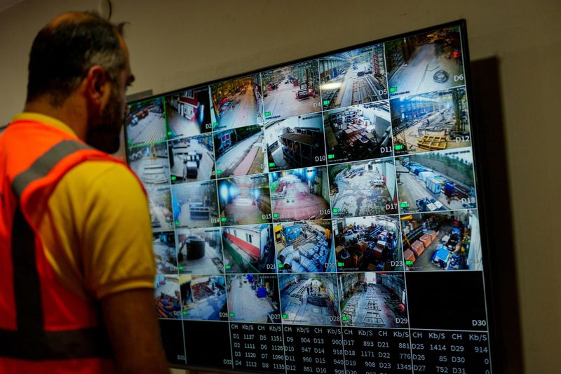 mature men discussing surveillance footages on huge screen while male operator using computer during work in security center