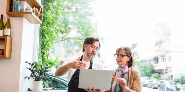 Man shows laptop to woman in cafe.