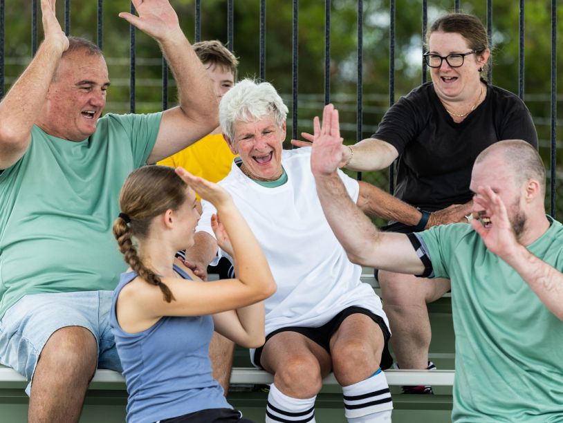 A diverse group happily high-fiving each other outdoors.