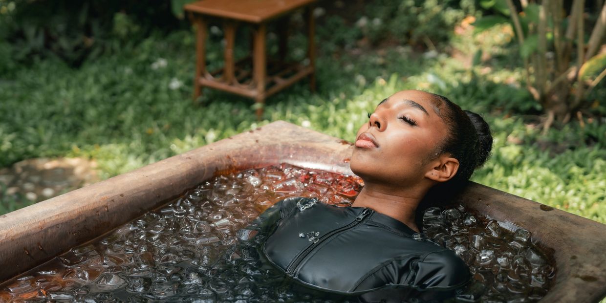 Woman relaxing in an ice-filled wooden tub outdoors.
