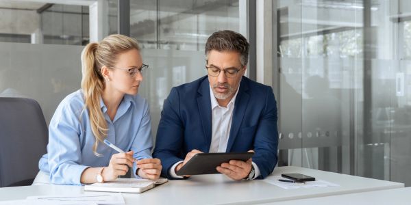 Two professionals discussing work using a tablet in a modern office.