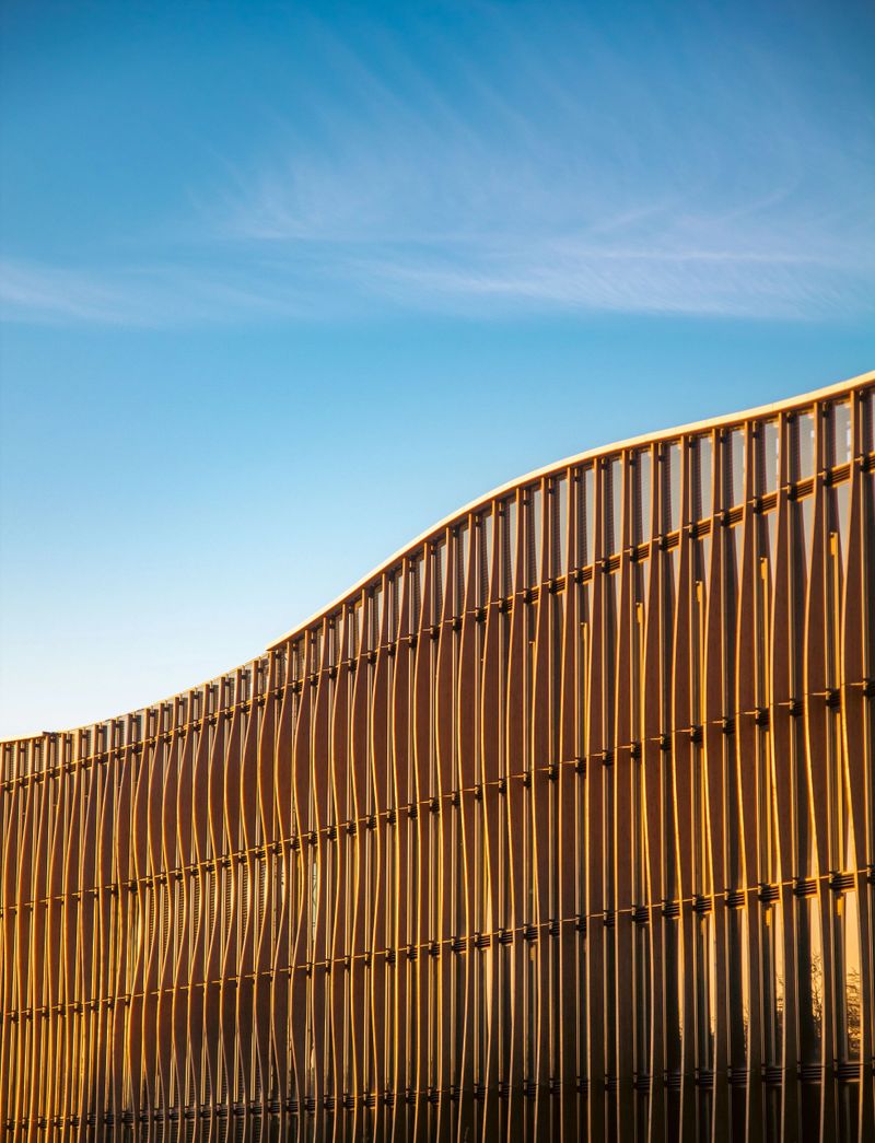 Modern architectural facade with wavy design against a clear blue sky, showcasing contemporary building aesthetics.