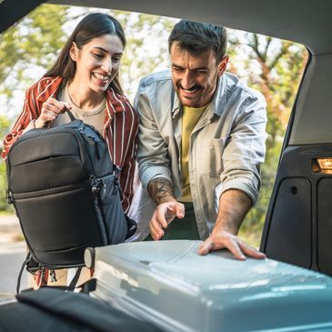 A happy couple loading luggage into a car trunk outdoors.
