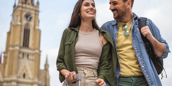 A happy couple sightseeing with luggage near a historic clock tower.