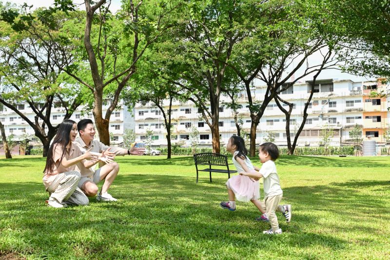 A family of four is playing in a park. The children are running around and the parents are watching them. Scene is happy and playful.