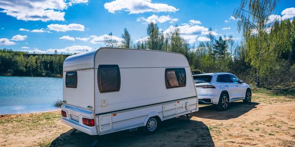 A white car towing a caravan near a lake under a blue sky.