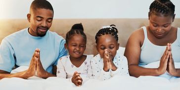 Family praying together with eyes closed and hands clasped.
