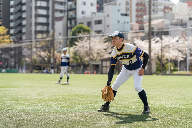 Players of a local baseball team are engaged in practice, showcasing teamwork and dedication in an urban park setting surrounded by blooming trees.
