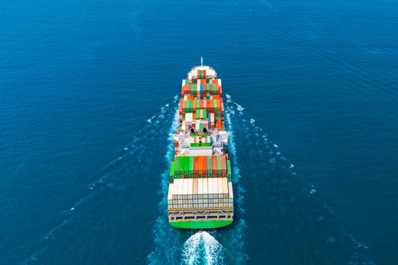 Giant container ship heavy ship goes on water with a lot of cargo in the sea strait when entering the port, rear back view directly from air from above