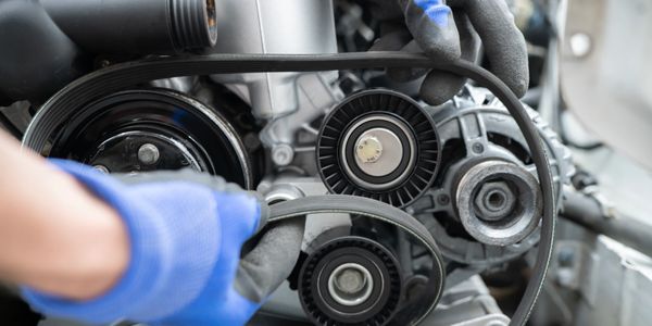 Mechanic fitting a new serpentine belt on a car engine.