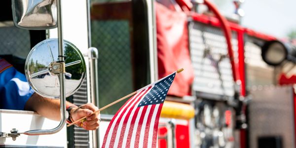 Person holding an American flag out of a fire truck window.