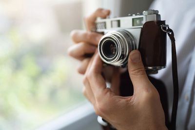 Close-up of hands holding a vintage camera near a window.