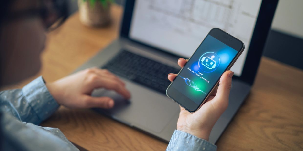 Persona usando chatbot en su teléfono frente a una computadora.